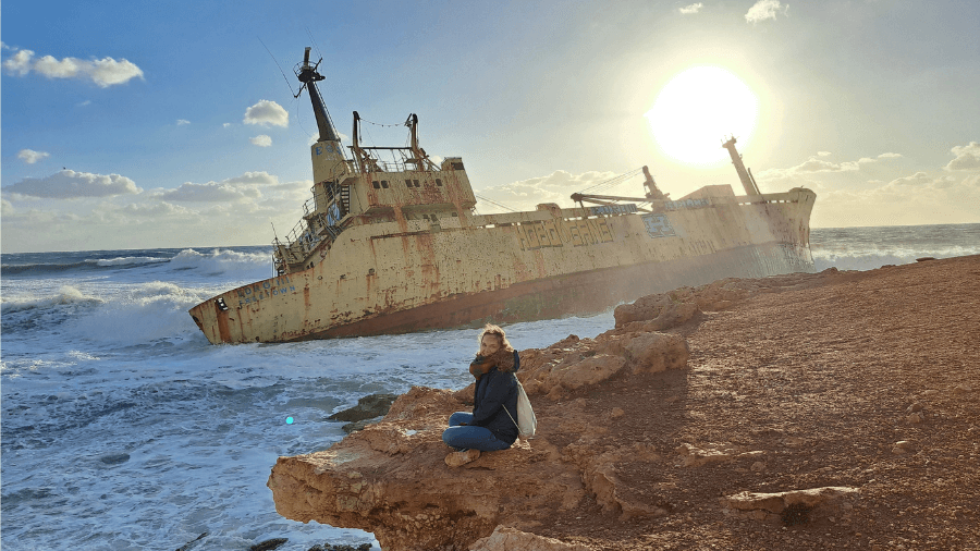 Frau sitzt vorm Schiffswrack Edro Zypern bei Sonnenuntergang