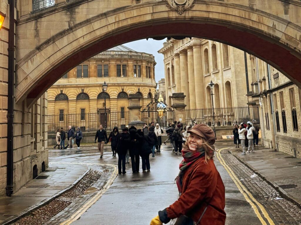 Das Bild steht sowohl für Oxford England als auch die zahlreichen Harry Potter Drehorte in England. Man sieht ein Mädchen mit einem britischen Hut die in den nassen Straßen von Oxford Sehenswürdigkeiten spaziert. Sie ist sehr glücklich und in einer dynamischen Bewegen. Die kamera hat aber ein Lächeln von ihr erwischt.