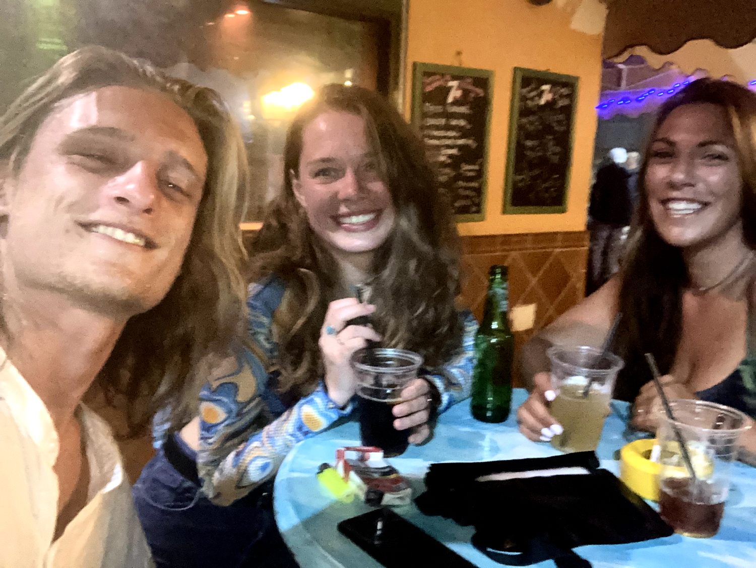 Das Bild steht wiedermal für die coolsten clubs in Corralejo: Kiwi und Bachata Clubs daneben. Eine Party auf Fuerteventura Party ist hier eine ganz andere Welt. Drei Menschen sitzen auf einem Bartisch draußen vor einem Club.