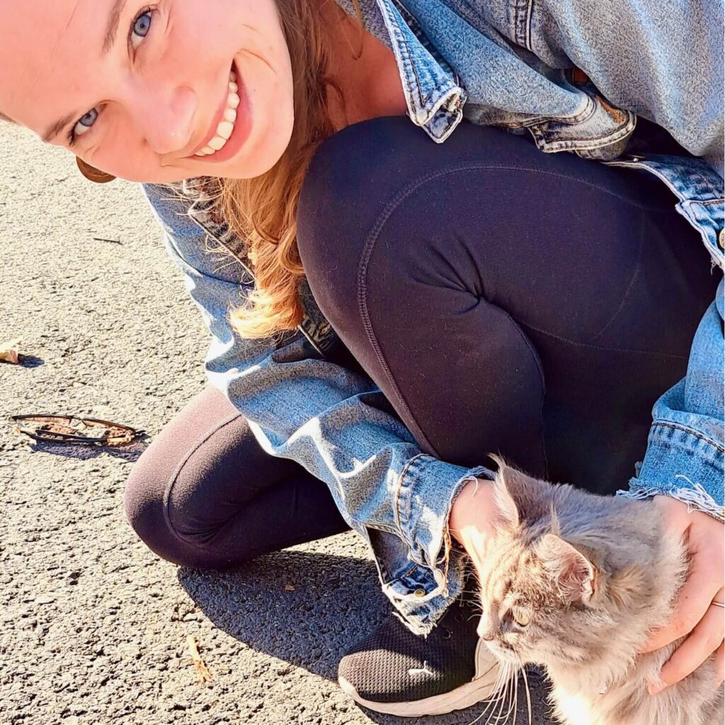 Me, a blonde girl, crouching next to a very fluffy grey cat of cyprus.
