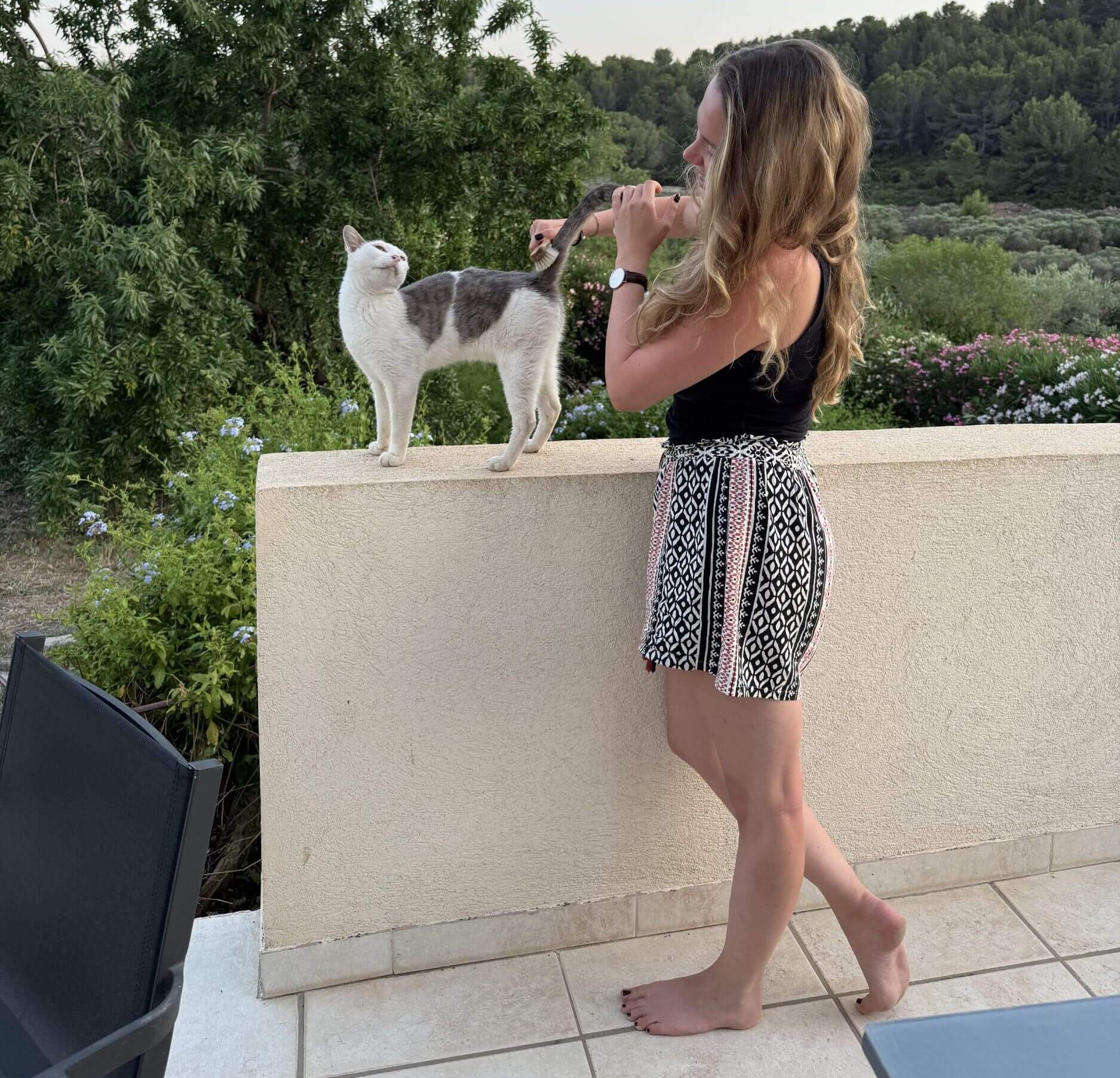 Hier sieht man mich, einer blonden Reisenden sich um die Katzen kümmern. Im Hintergrund sieht man die die Pinienwälder der Provence.
