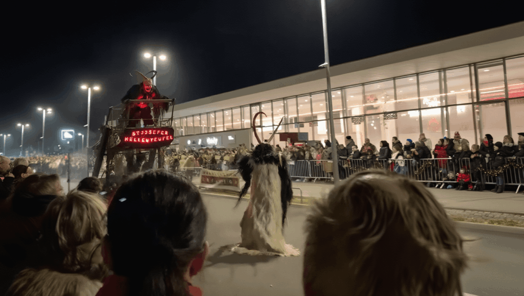 Auf diesem Bild sieht man einen Perchtenlauf. Krampus, Perchten und ein umgebautes Auto mit Turm fahren hier wild durch die Straßen von Österreich.