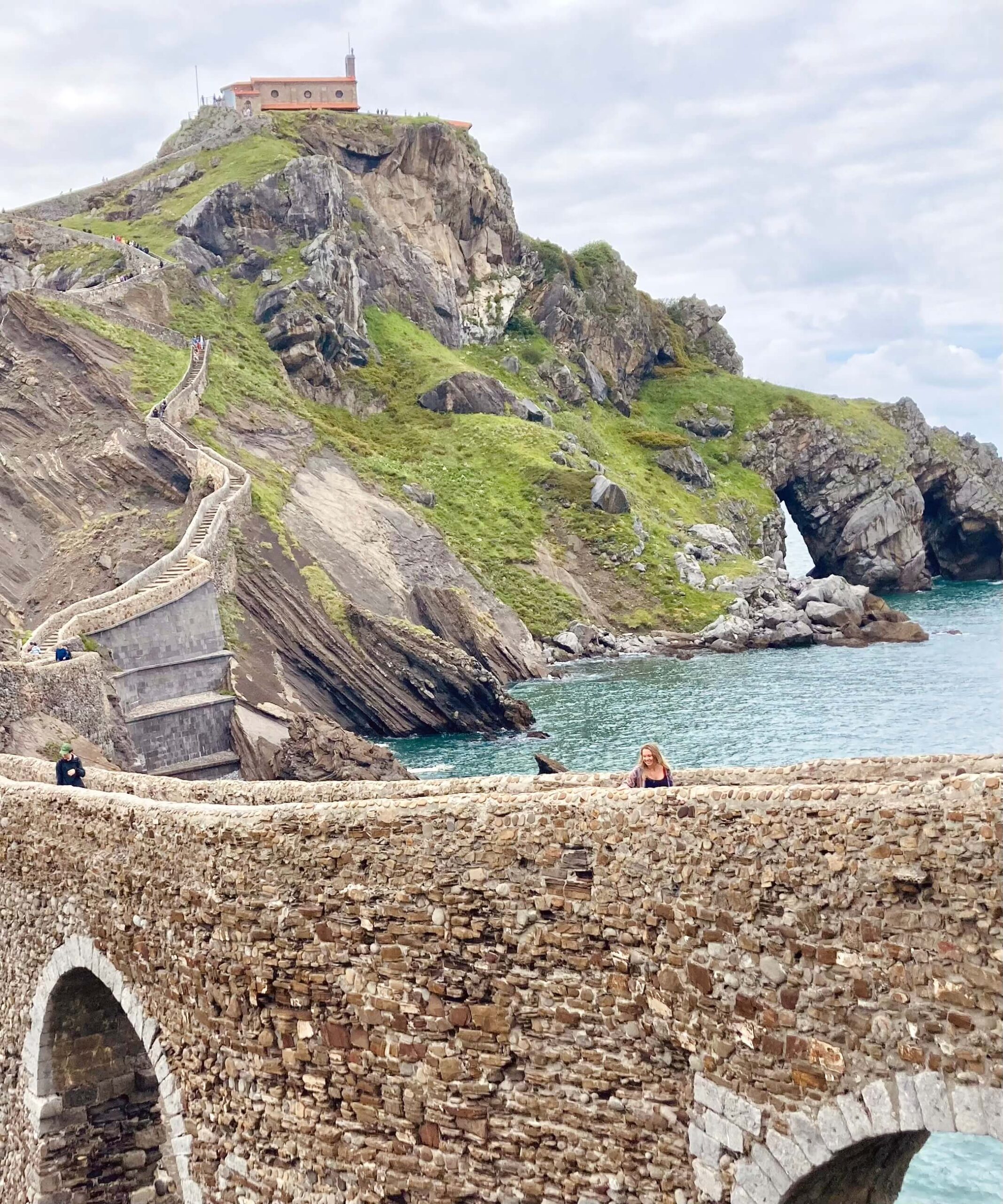 Man sieht San Juan de Gaztelugatxe eine Kirche auf einem Berg in Nordspranien am See. Es führt eine lange Treppe hinauf. Ein perfekter Tagestrip für surfen in spanien.