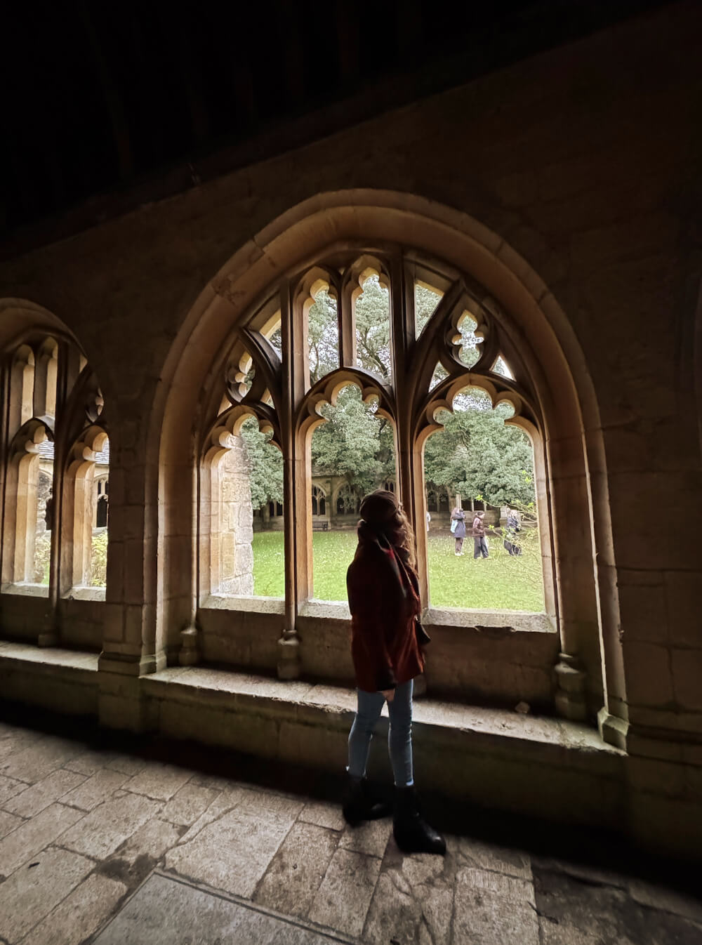 The photo shows another Harry Potter Oxford filming location. A woman is walking through the cloisters of New College, and in the background she is looking toward the tree where Draco Malfoy was transformed into a ferret. It is one of the most beautiful Oxford attractions.