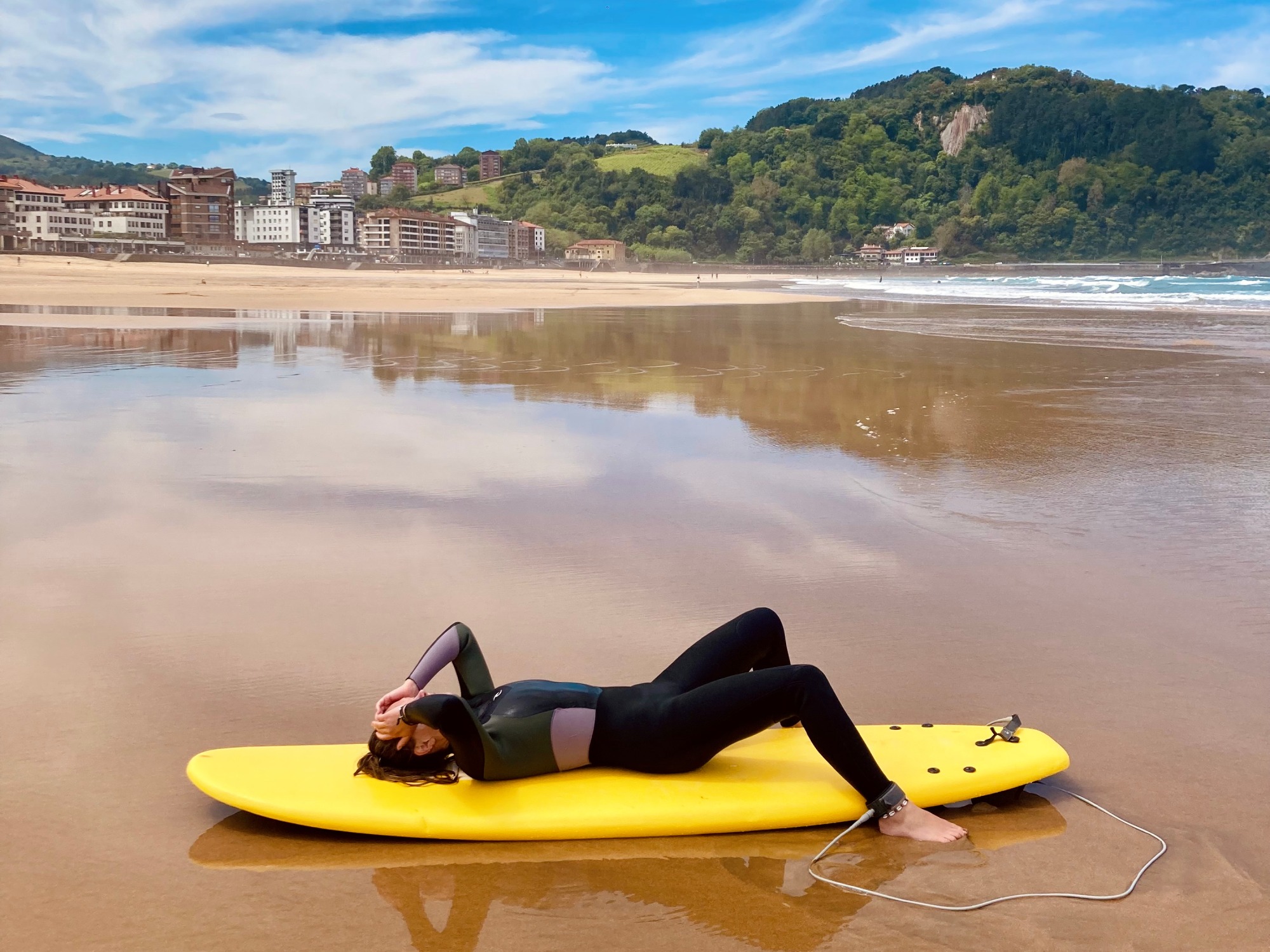 Girl is exhausted after surfing in Spain in Spanish basque country. She is laying on her Board at the beach and holding her head