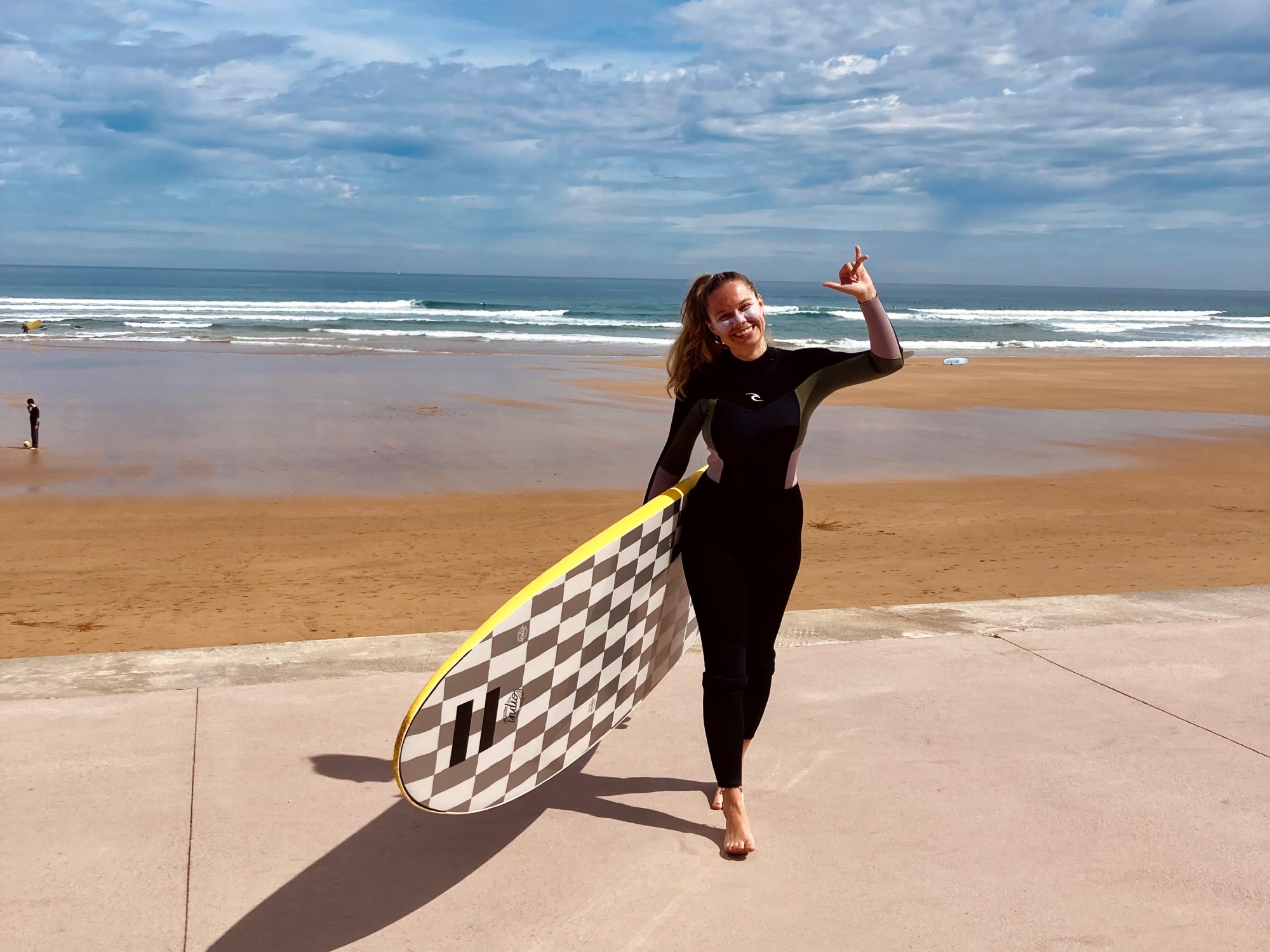 A girl in a wetsuit holding a surfboard. she is surfing in spain in the spanish basque country.